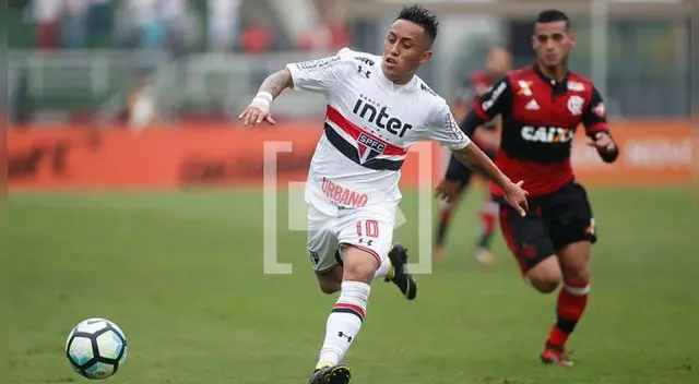 Christian Cueva conduce un balón, Miguel Trauco lo mira desde atrás.