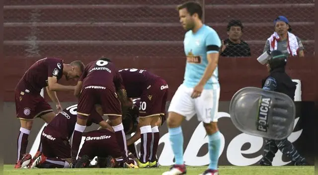 Renzo Revoredo sufre mientras los jugadores de Lanús celebran un gol. Renzo Revoredo sufre mientras los jugadores de Lanús celebran un gol.