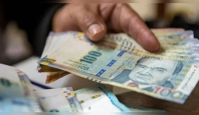 Sujeto agarrando con su manos varios billetes de 100 soles.