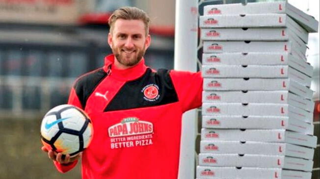 Chris Neal posa con una sudadera con publicidad de Papa Johns y al lado de una torre de caja de pizzas