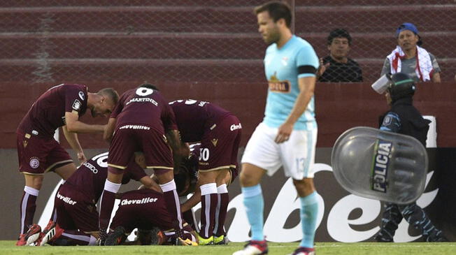 Renzo Revoredo sufre mientras los jugadores de Lanús celebran un gol.